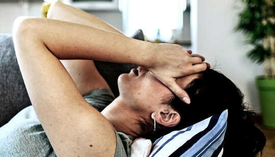 یک زن در حالی که دستانش را روی صورتش گذاشته است روی یک کاناپه دراز کشیده است