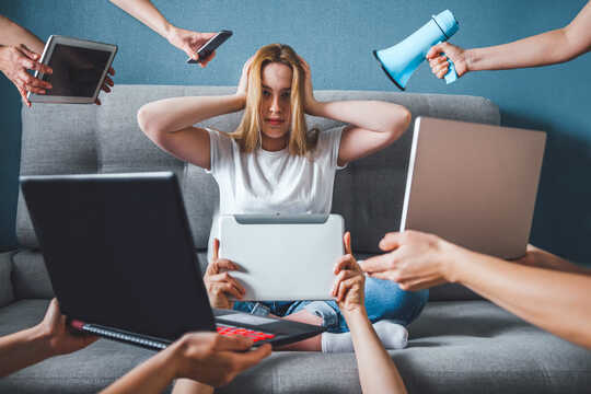 Wanita duduk dengan tangan di telinganya seperti megafon, telefon bimbit, 2 komputer riba, 2 iPad didorong ke wajah
