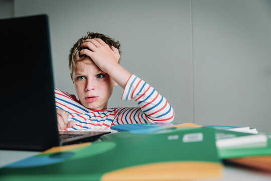 Anak laki-laki melihat layar komputer dengan tangan di rambut, berpikir.