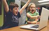 kaksi lasta tietokoneen edessä juhlimassa menestystä kädet ilmaan ja suuret hymiöt