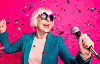 γκριζομάλλα γυναίκα φορώντας funky ροζ γυαλιά ηλίου τραγουδώντας κρατώντας ένα μικρόφωνο