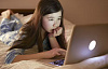 웹캠을 보고 노트북을 사용하여 침대에 누워 있는 어린 소녀