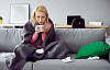 uma mulher sentada enrolada em um cobertor bebendo uma bebida quente