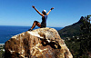 escursionista seduto in cima a un'enorme roccia con le braccia alzate in aria in trionfo