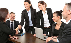 femmes se serrant la main lors d'une réunion d'affaires, avec des hommes regardant