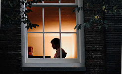 persona sentada sola en una casa, vista a través de una ventana