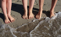paar voeten staan ​​op het strand aan de rand van de golven die naar de kust komen