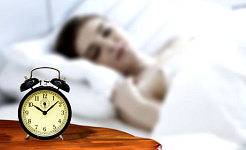egy nő, aki egy régi stílusú, nem elektronikus ébresztőórával alszik az éjjeliszekrényen