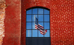 a US flag seen through a window in a red brick wall