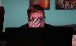 a man sitting in front of a computer screen rubbing his eyes