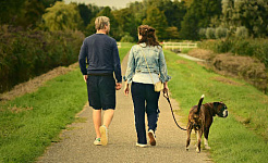 mann, kvinne og hund i bånd som går nedover en sti