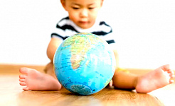 một đứa trẻ ngồi trên sàn chơi với quả địa cầu