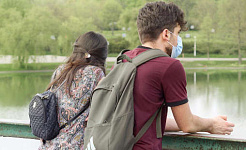 um jovem casal, usando máscaras protetoras, em pé em uma ponte