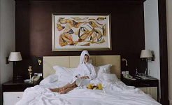 a person sitting up in a hotel bed having breakfast in bed