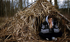 fiatalember meditál egy szalmamenhely előtt