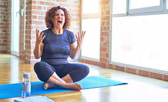 kvinne som sitter på en yogamatte med hendene oppe i frustrasjon og skrik