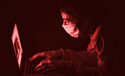 en person som bär en kirurgisk mask som arbetar vid en dator
