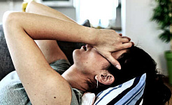 یک زن در حالی که دستانش را روی صورتش گذاشته است روی یک کاناپه دراز کشیده است