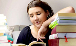 a young woman peacefully reading a book with her arm resting a whole stack of books
