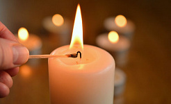 ένα χέρι που ανάβει ένα κερί, με άλλα αναμμένα κεριά στο βάθος