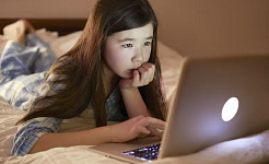 一個年輕女孩躺在床上，在網絡攝像頭的注視下使用筆記本電腦