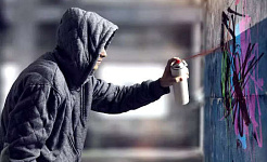 ένας νεαρός άνδρας φορώντας κουκούλα ψεκάζοντας γκράφιτι σε έναν τοίχο
