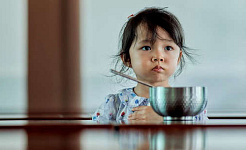 کودک ناراضی که جلوی ظرف غذا نشسته است