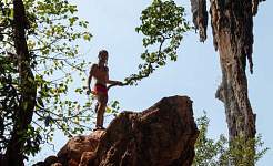 egy fiatal fiú felmászik egy sziklaképződmény tetejére