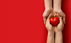 молодые руки держат светящийся красный камень в форме сердца