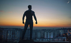 siluet seorang pria dengan tangan terkepal berdiri di atas atap yang menghadap ke kota