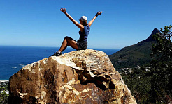 wandelaar zittend op de top van een enorme rots met de armen in de lucht in triomf