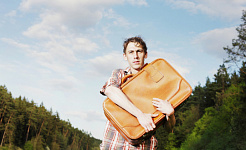 mężczyzna stojący na zewnątrz, przyciskając walizkę do piersi
