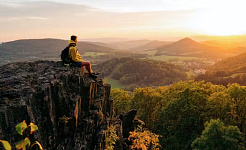 کوهنوردی که بر روی صخره ای در طبیعت نشسته است