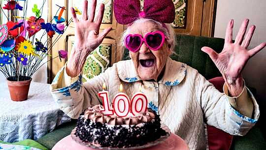 Một người phụ nữ trông rất phấn khích với cặp kính màu hồng và đeo một chiếc nơ, đang nhìn vào chiếc bánh với