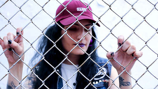 девушка в бейсболке стоит за забором из звеньев цепи
