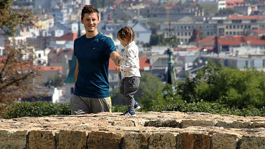 ett litet barn som går på toppen av en stenmur med pappa stående genom att le och hålla barnets hand