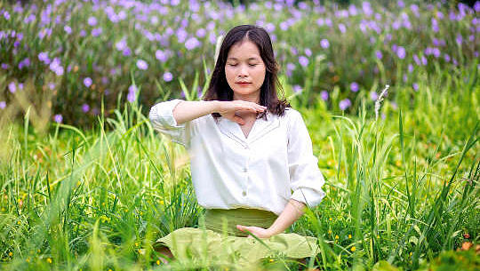 a woman sitting with eyes closed in a meadow