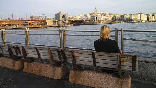 donna seduta da sola su una panchina di fronte all'acqua e allo skyline della città