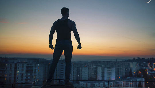 силуэт человека со сжатыми кулаками, стоящего на крыше с видом на город