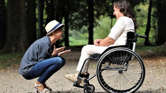 omtänksam person som sitter på huk framför en annan i rullstol