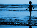 졸졸 흐르는 파도의 가장자리에 있는 물 속에 서 있는 어린 소년