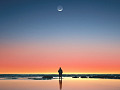 איש עומד על שפת הים מול רסיס דק של ירח