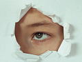 A person looking through a punched-out hole in a sheet of paper. Image by Victoria from Pixabay. 