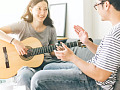 एक महिला अपने साथी के सामने बैठकर गिटार बजा रही है