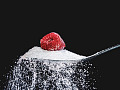 et bringebær som sitter på toppen av en teskje sukker