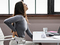 Woman sitting at a computer with her hand on her aching back. Image by fairpharma from Pixabay. 