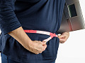 en person, der måler sig selv rundt om taljen, mens han holder en digital vægt under armen