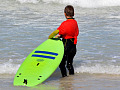 समुद्र के किनारे बॉडी सर्फिंग बोर्ड पकड़े खड़ा बच्चा