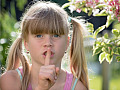 ein junges Mädchen mit dem Finger über dem Mund im universellen Symbol „Stille, sei still“
