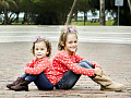 kaksi hymyilevää nuorta sisarta istuu seläkkäin